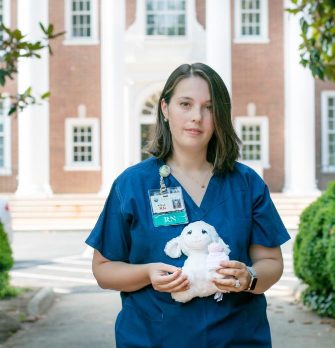 Caregiver holding stuffed animal in front of hospital blurred background