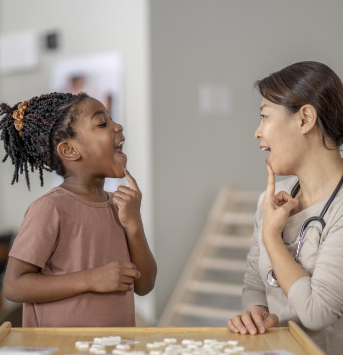 A therapist guides a young girl through speech therapy exercises using a playful and modern approach.
