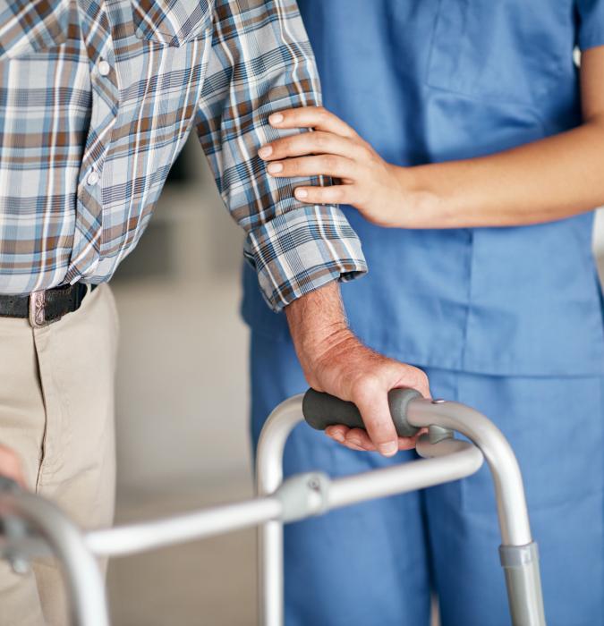 Caregiver assisting her elderly rehab patient who's using a walker for suppor