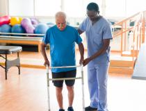 Male Caregiver walking with rehabilitation patient in exercise rehab room