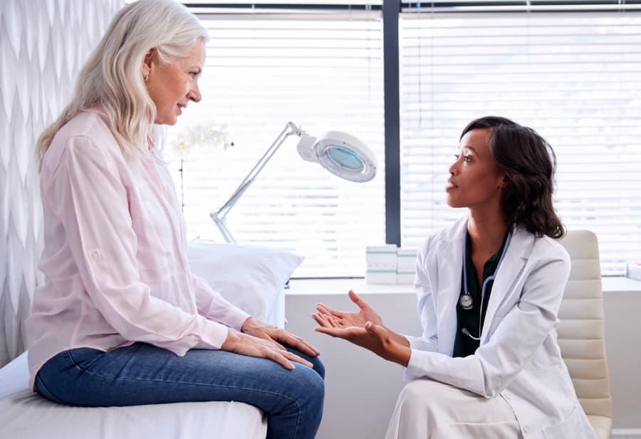 Doctor sitting on a stool talking with female patient in examination room