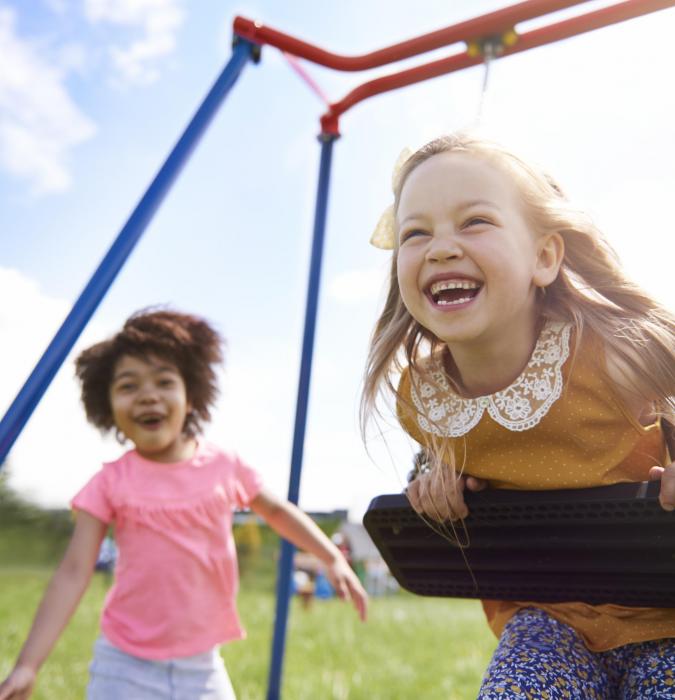 Two small children laughing and playing on a swing set 
